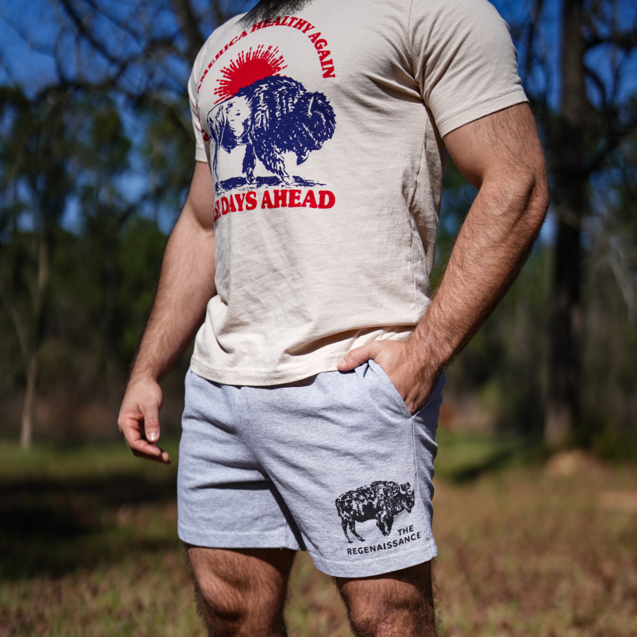 A person stands outside among trees and grass wearing the Farm Fresh Clothing Best Days Ahead MAHA Tee, a beige t-shirt featuring a bison graphic and text that celebrates regenerative agriculture.