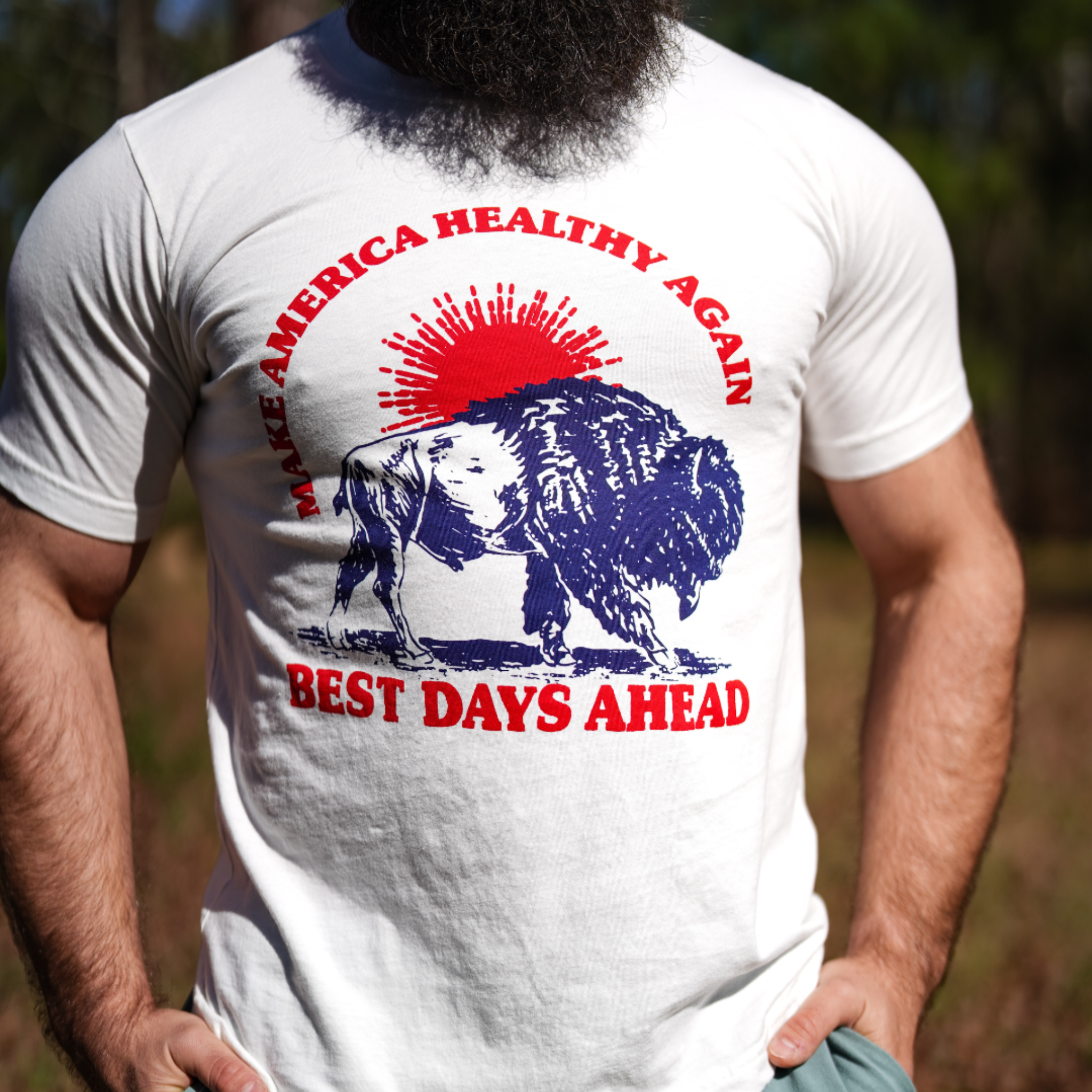 A person wears the Farm Fresh Clothing Best Days Ahead MAHA Tee, a made-in-USA white shirt with a bison in front of a red sunburst and the phrases MAKE AMERICA HEALTHY AGAIN and BEST DAYS AHEAD in bold red and blue letters.