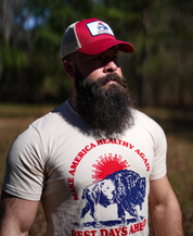 A bearded man wears the Farm Fresh Clothing Best Days Ahead MAHA Trucker Hat and a Make America Healthy Again, Best Days Ahead bison T-shirt, standing outdoors in sunlight with trees—embracing regenerative agriculture.