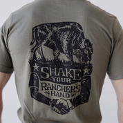 A person wears the Farm Fresh Clothing Bison Ranchers Handshake Tee, made from organic cotton, with a black cow-on-grass graphic above Shake Your Ranchers Hand and two hands shaking—ideal for transparent food system fans.