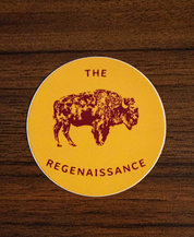 The Regenaissance Sticker by Sticker Mule is a round yellow vinyl sticker with a maroon Great American Bison and THE REGENAISSANCE in maroon, shown on a wooden surface.