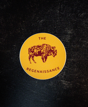 The Regenaissance Sticker by Sticker Mule is a circular yellow vinyl sticker with a maroon Great American Bison illustration and THE REGENAISSANCE in maroon, shown on a dark textured background.