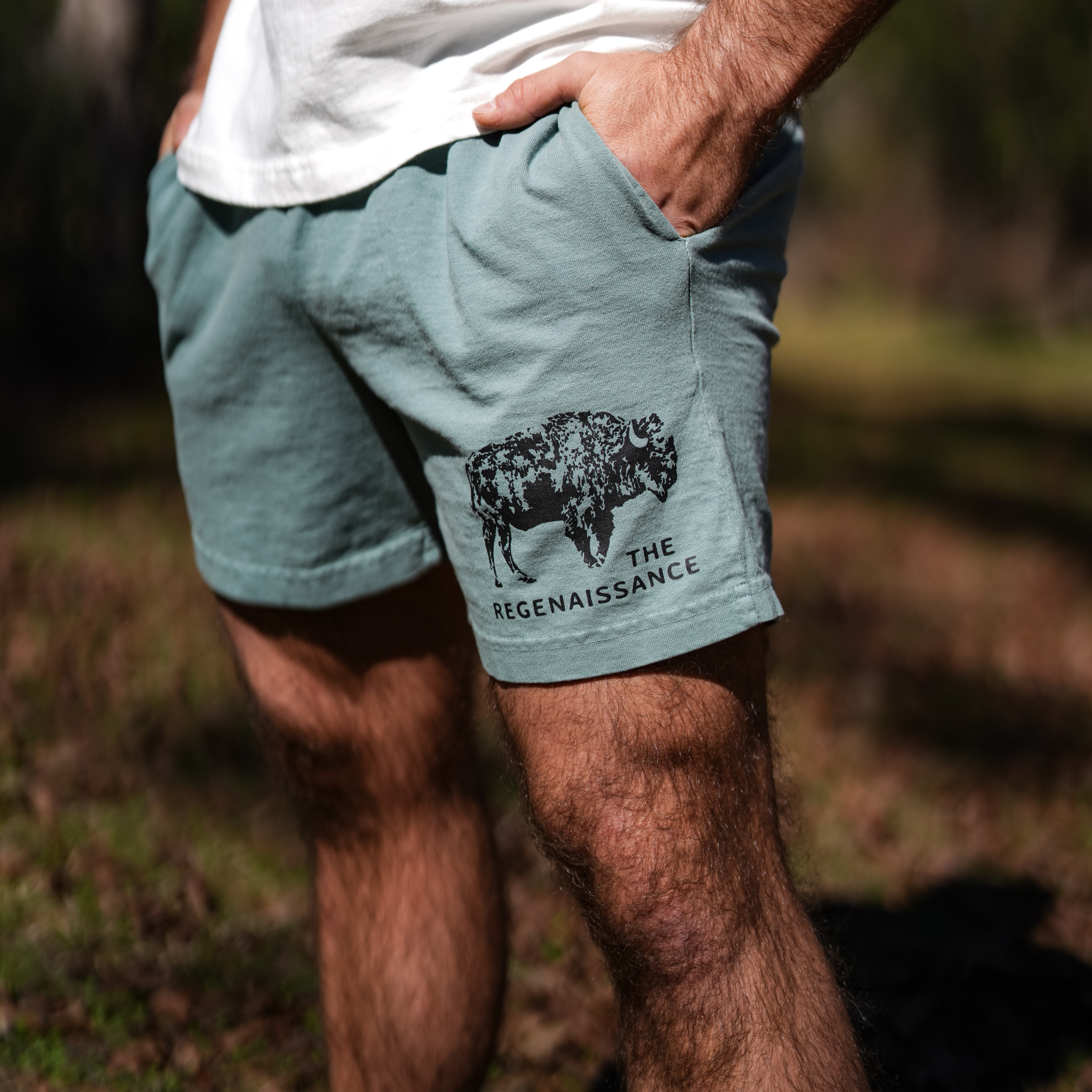 A person wears Los Angeles Apparel Men's Bison Shorts in light green, featuring a black buffalo graphic and "The Regenaissance" text—perfect for anyone embracing regenerative living.