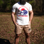 A bearded man stands outdoors on leaf-covered ground, wearing a white tee with "AMERICA HEALTHY AGAIN, BEST DAYS AHEAD" and a bison, paired with Los Angeles Apparel Men's Bison Shorts—ideal for fans of regenerative agriculture.