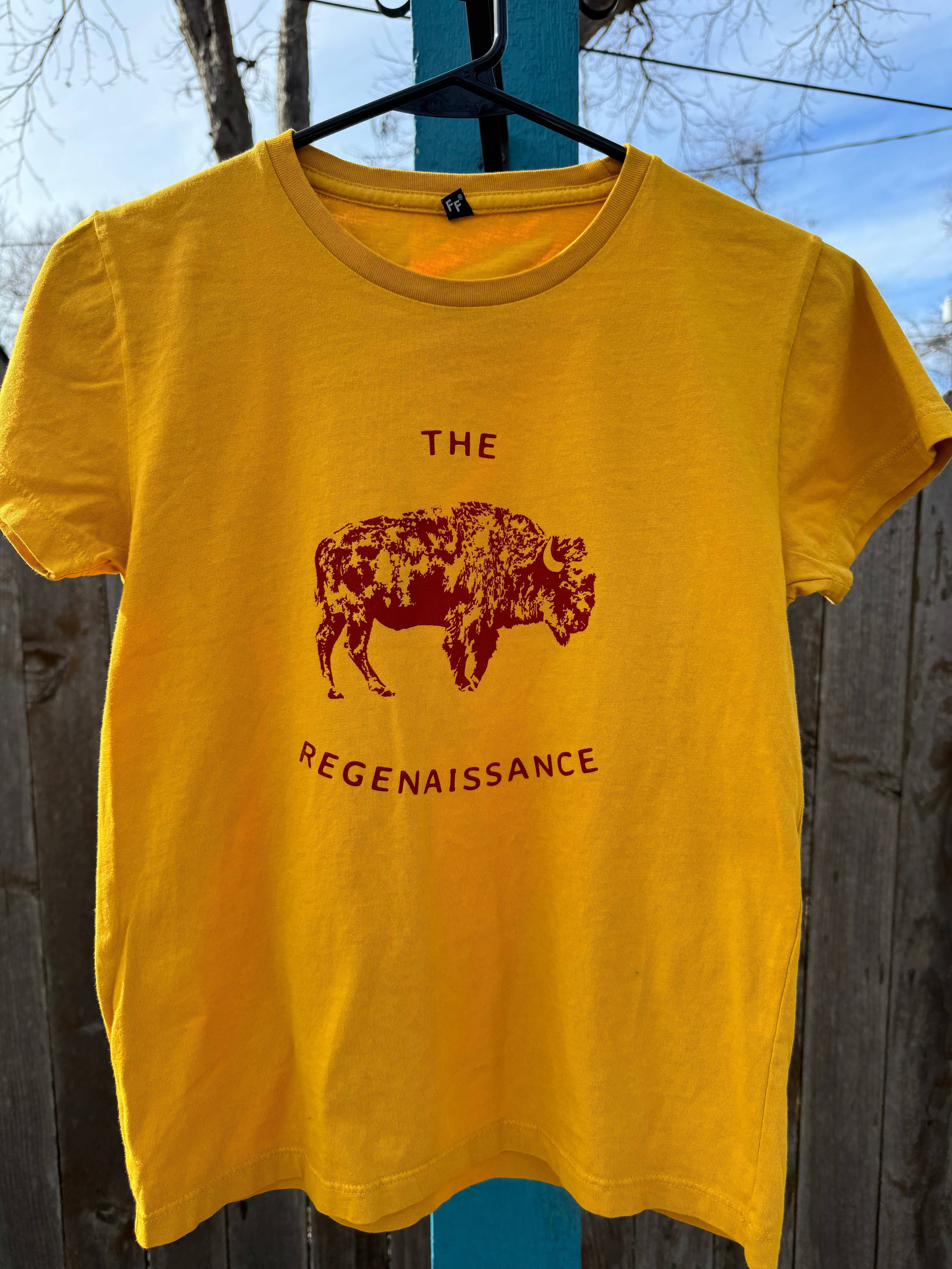 A yellow Kids OG Bison Tee by Farm Fresh Clothing hangs outdoors on a hanger, featuring a maroon bison graphic above THE REGENAISSANCE. Made in the USA from organic cotton, its inspired by regenerative agriculture.
