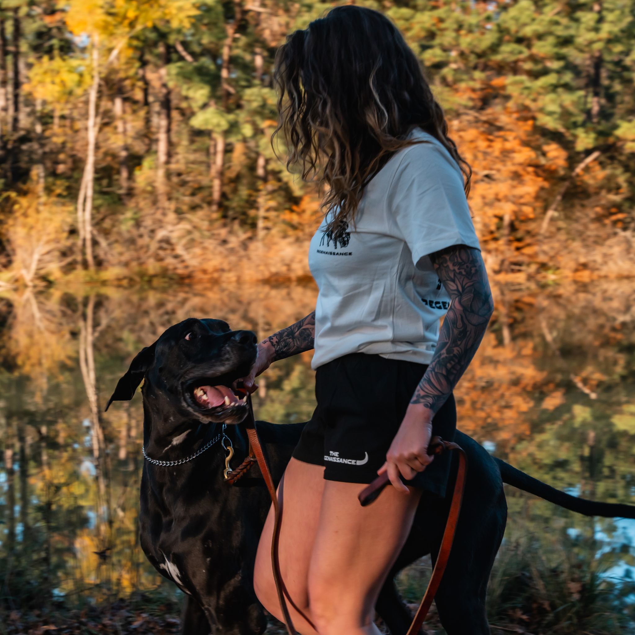 Wearing Los Angeles Apparel Womens Longhorn Shorts, a woman stands by a lake with her dog, showcasing harmony inspired by regenerative agriculture.