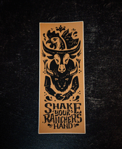 The Shake Your Ranchers Hand Sticker by Sticker Mule is a rectangular vinyl sticker featuring a black cow skull in a cowboy hat, fish above, and “SHAKE YOUR RANCHER’S HAND” below on a dark textured background.