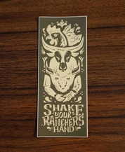 The Shake Your Ranchers Hand Sticker by Sticker Mule features a green design with a cows head, cowboy hat, handshake, and Shake Your Ranchers Hand text—encouraging support for farmers and real food. Shown on rustic wood.