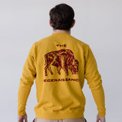 Wearing Farm Fresh Clothing’s Bison Crewneck Sweatshirt in yellow with a bold maroon bison and “THE REGENAISSANCE” on the back, this eco-friendly, organic cotton piece highlights sustainable style against a simple backdrop.
