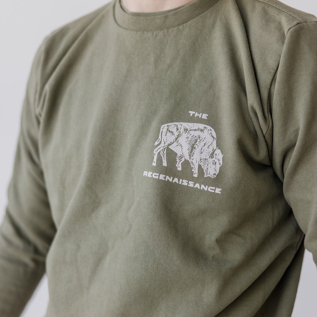 A person wears the Farm Fresh Clothing Bison Crewneck Sweatshirt in olive green, featuring an organic cotton build, a buffalo graphic, and THE REGENAISSANCE text; their face is partially out of frame.