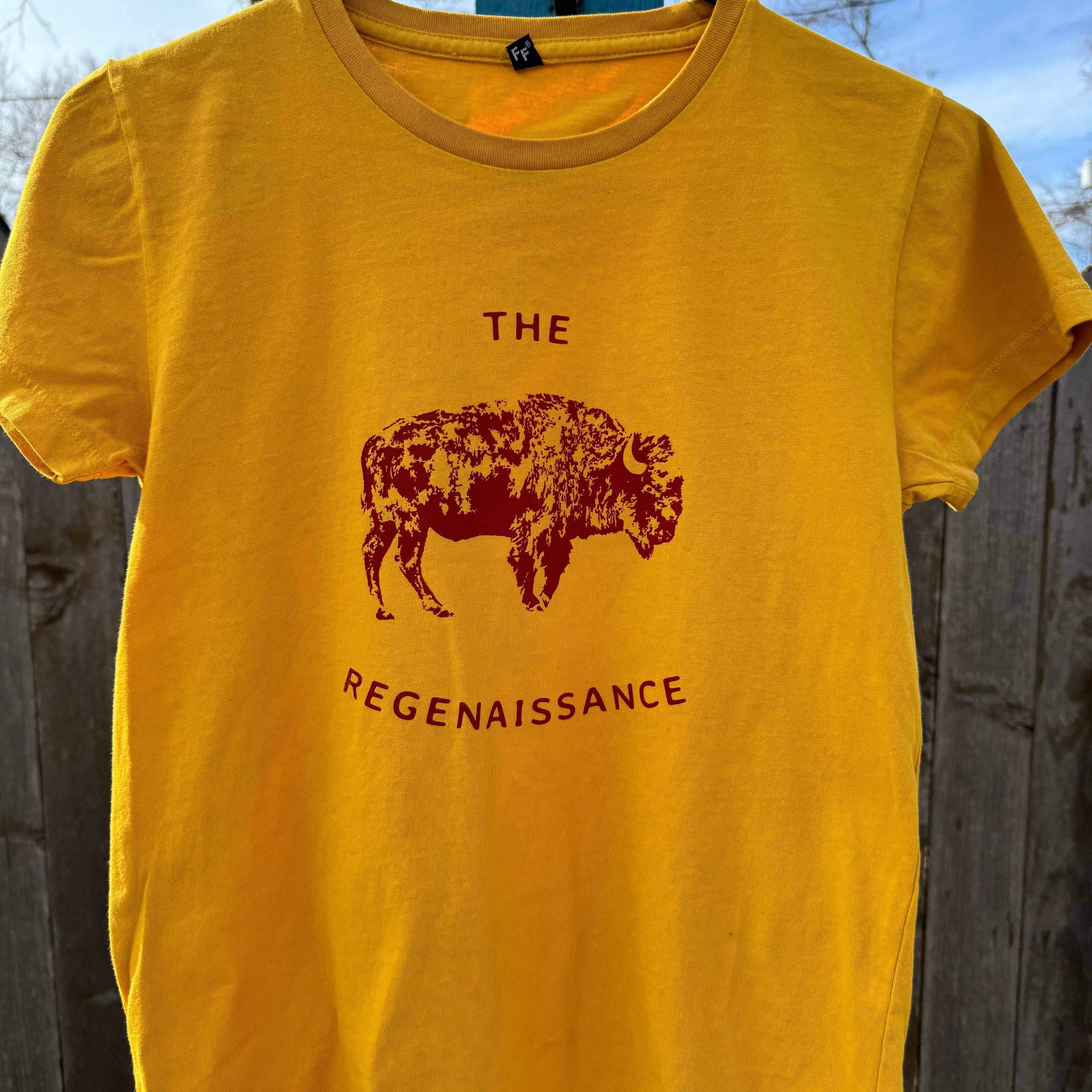 A yellow Kids OG Bison Tee by Farm Fresh Clothing hangs outdoors on a hanger, featuring a maroon bison graphic above THE REGENAISSANCE. Made in the USA from organic cotton, its inspired by regenerative agriculture.