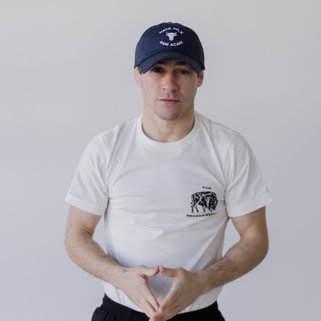 Wearing the Farm Fresh Clothing MMRA Cow Cap, a white T-shirt with a small chest graphic, and black pants, a person stands against a plain light background with hands forming a triangle shape.