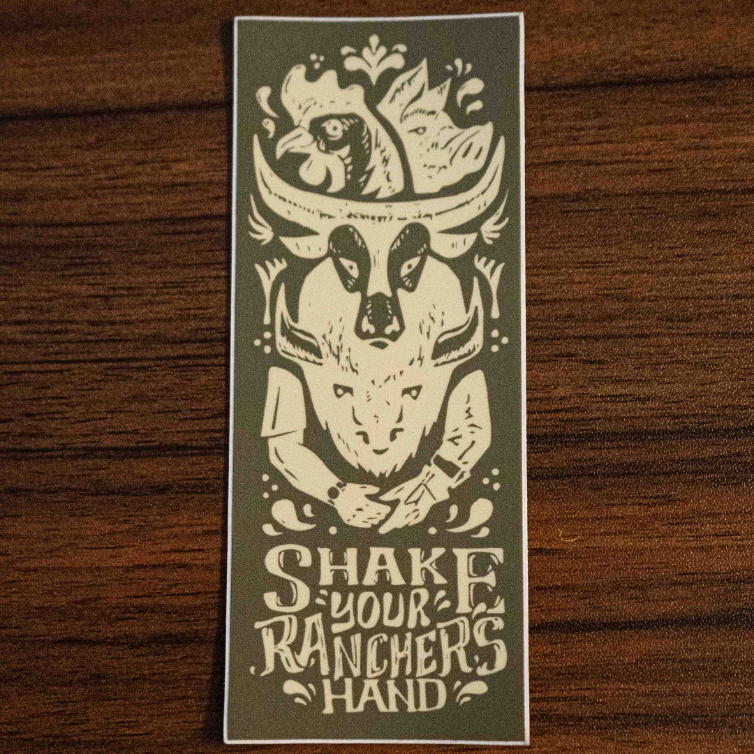 The Shake Your Ranchers Hand Sticker by Sticker Mule features a green design with a cows head, cowboy hat, handshake, and Shake Your Ranchers Hand text—encouraging support for farmers and real food. Shown on rustic wood.