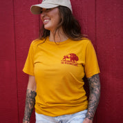 Woman smiling in mustard Regenerate Agriculture Tee, front view, with red bison and The Regenaissance logo.