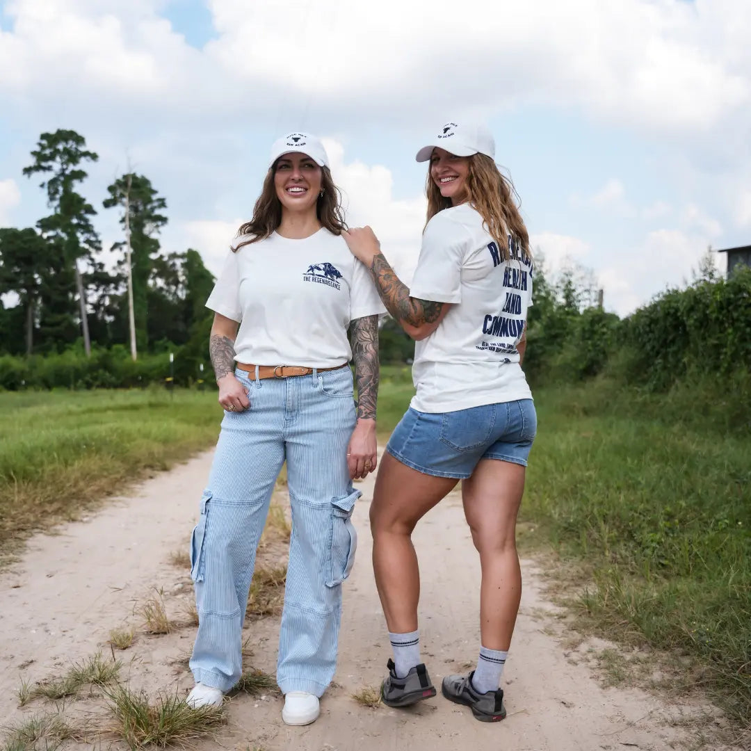 Two women smiling in eggshell Regenerate Agriculture Tees, one showing the front bison logo, the other showing back print “Regenerate Health Land Community.”