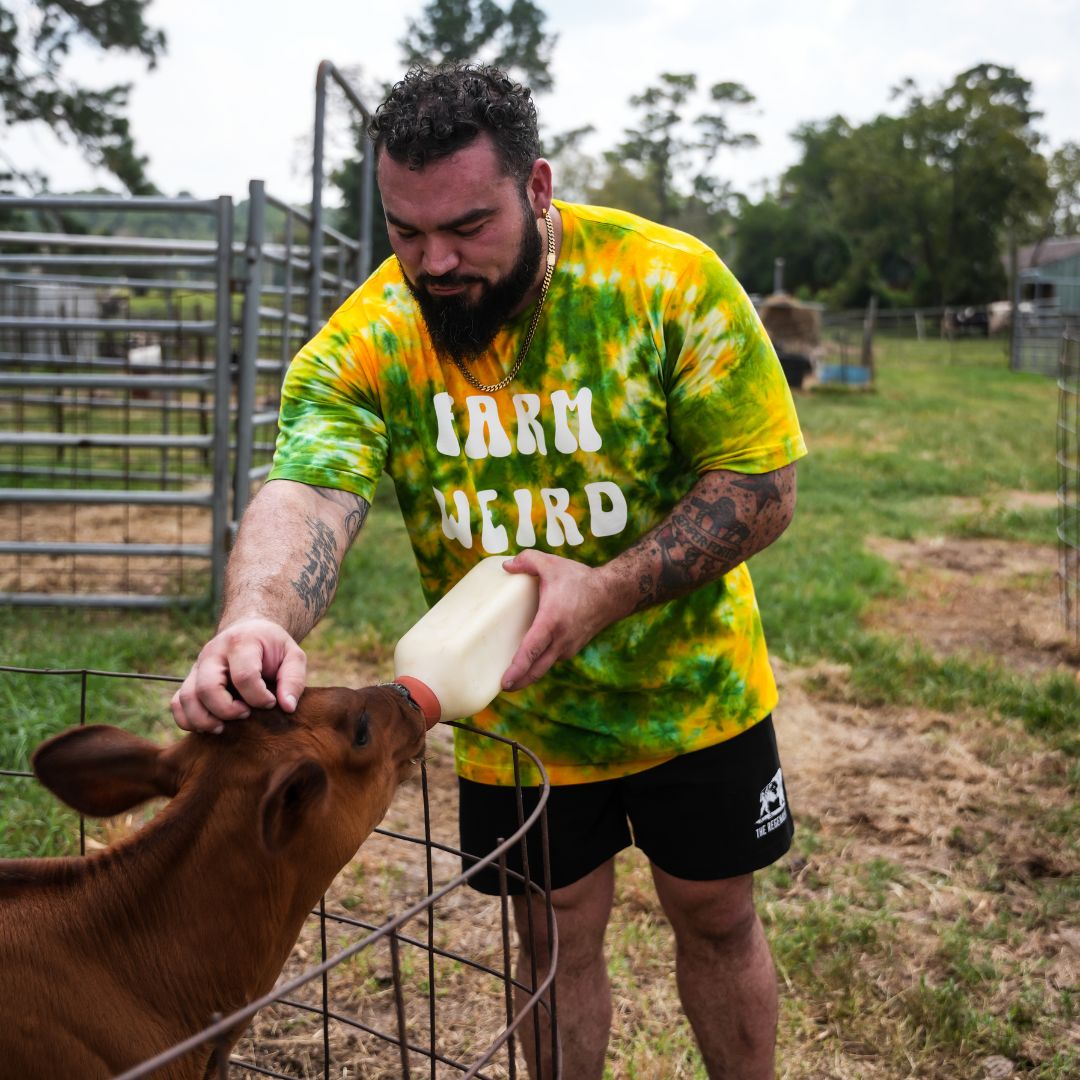 Male model wearing black Regen Men’s Shorts in an outdoor setting, showcasing athletic fit and minimalist design while feeding a calf