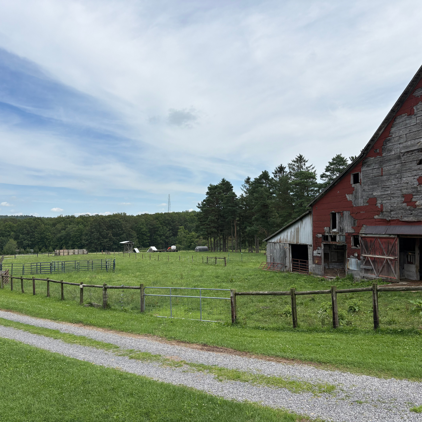 Red barn with a gravel path and green field under a blue sky with clouds.