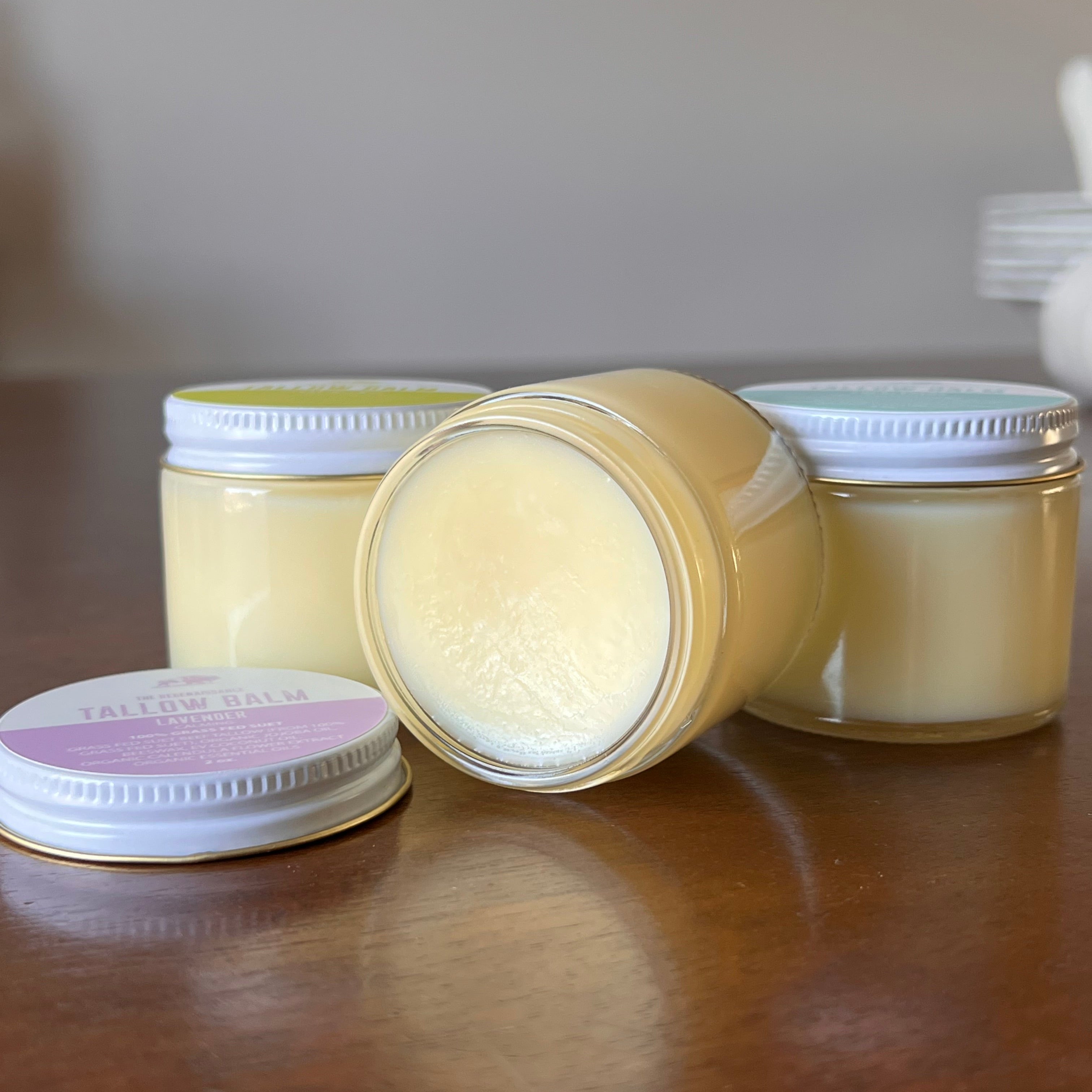 Jar of Lavender Tallow Balm with lid off on a wooden shelf in front of two other jars of tallow balm