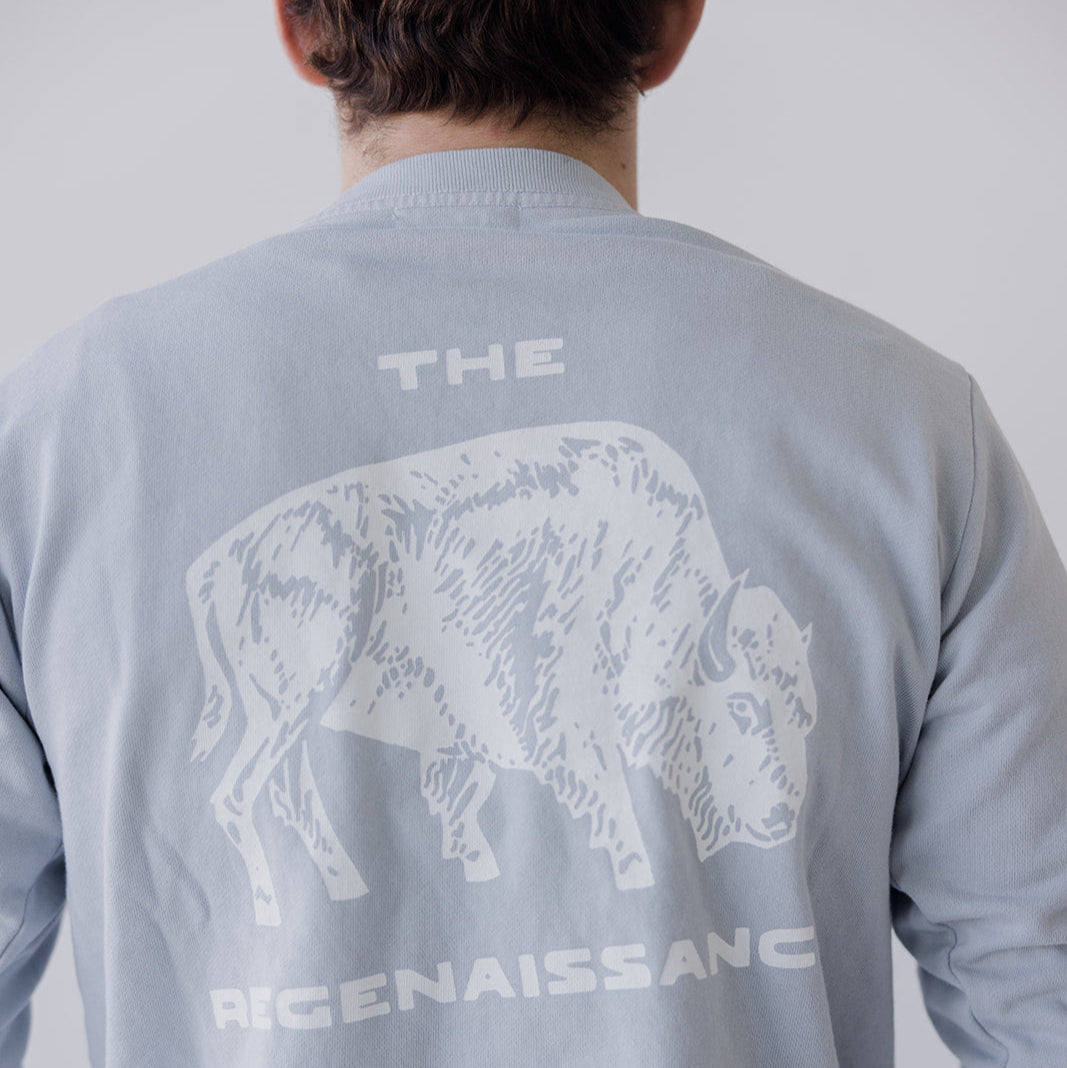 A person, shown from behind, wears the Farm Fresh Clothing Bison Crewneck Sweatshirt in light gray—an organic cotton top featuring a white bison graphic and THE REGENAISSANCE on the back, embodying sustainable values.