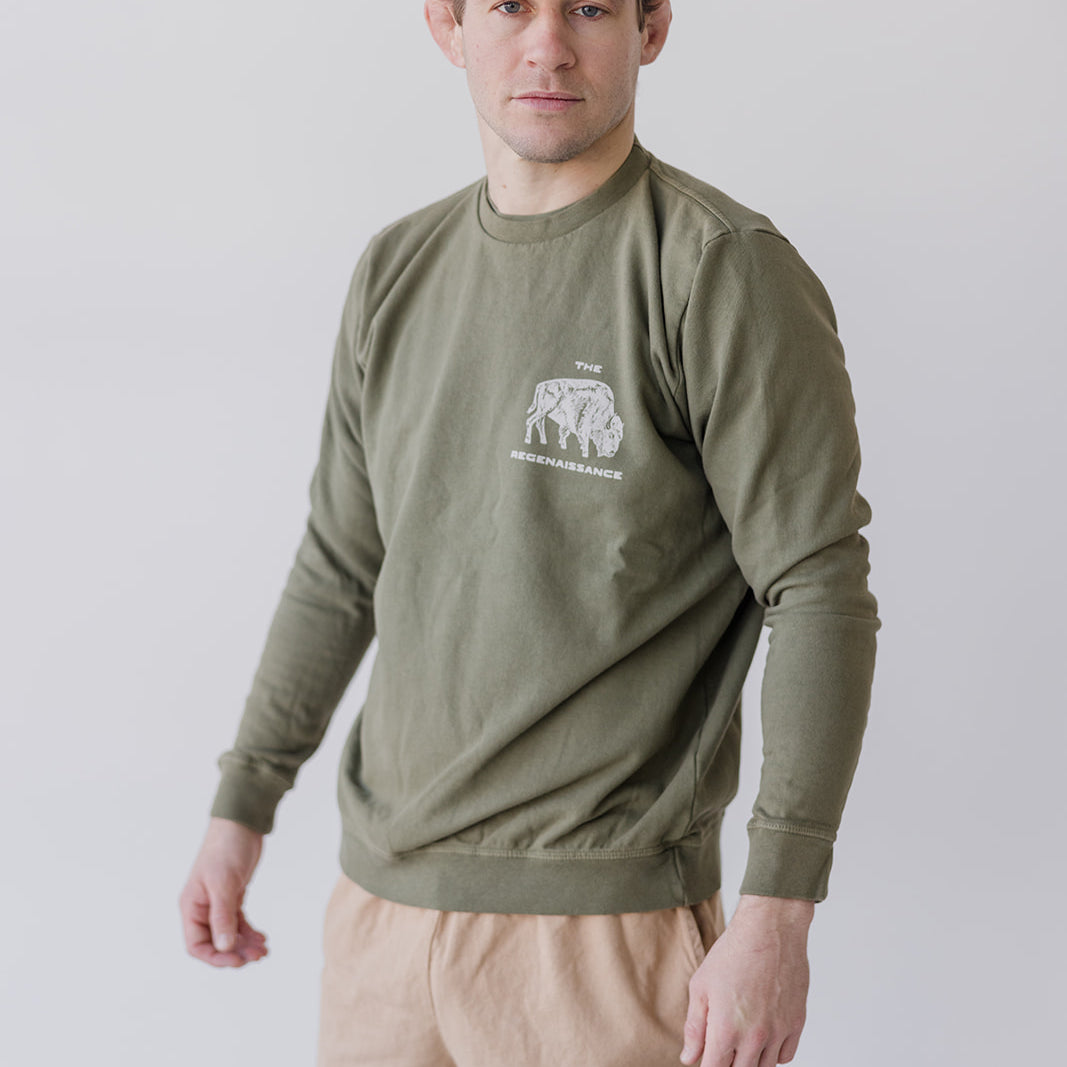 A man wears a rosemary Bison Crewneck Sweatshirt by Farm Fresh Clothing and beige shorts with a bison logo, standing against a plain white background.